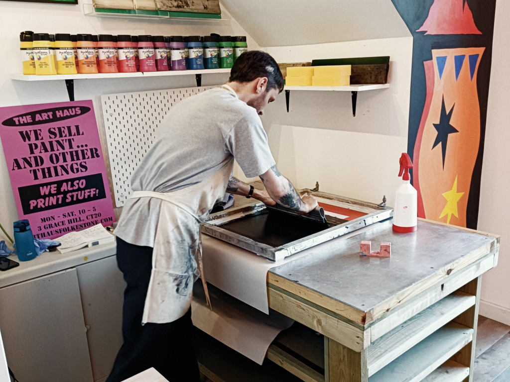 A person works at a printing station, preparing for a screen print.