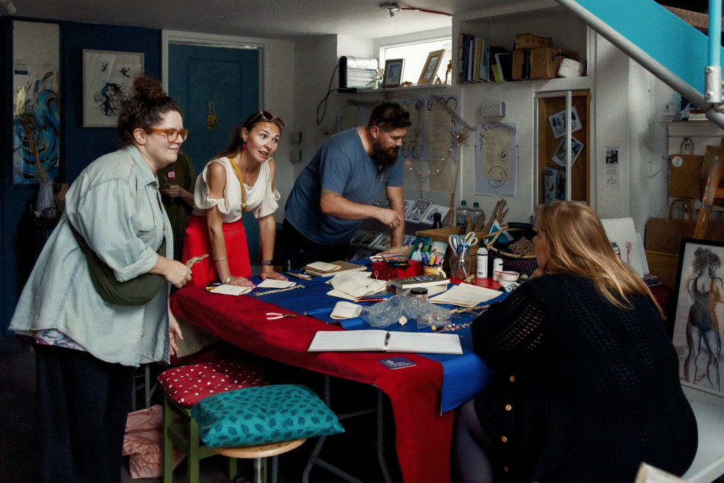 Four people are engaged in an art workshop around a table filled with art supplies in an inviting studio space.
