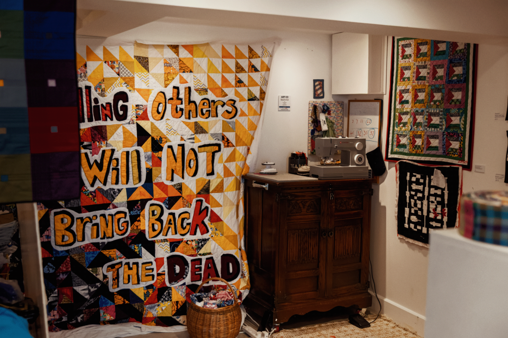 A quilt hangs on the wall with the text "Killing Others Will NOT Bring Back the Dead"