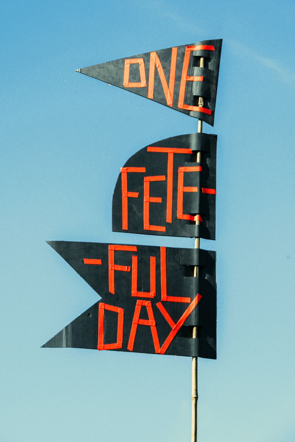A handmade sign pictured against the blue sky reads "one fete, full day"